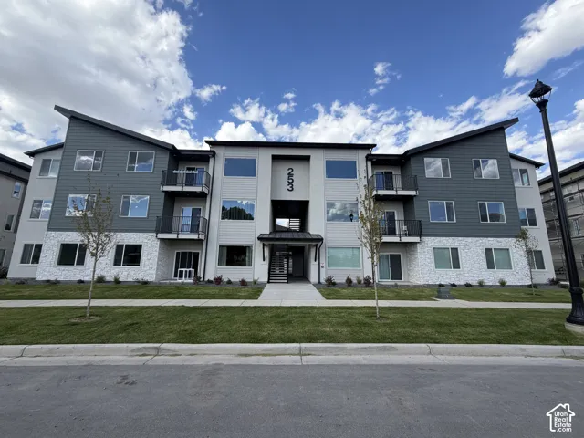 Modern multi-story building featuring a pitched roofline, stone veneer accents, and multiple balconies with metal railings