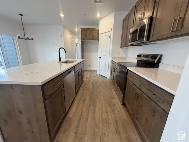 Kitchen featuring wood-finish flooring, white countertops, dark wood-tone cabinetry, stainless steel appliances, and an island with an integrated sink