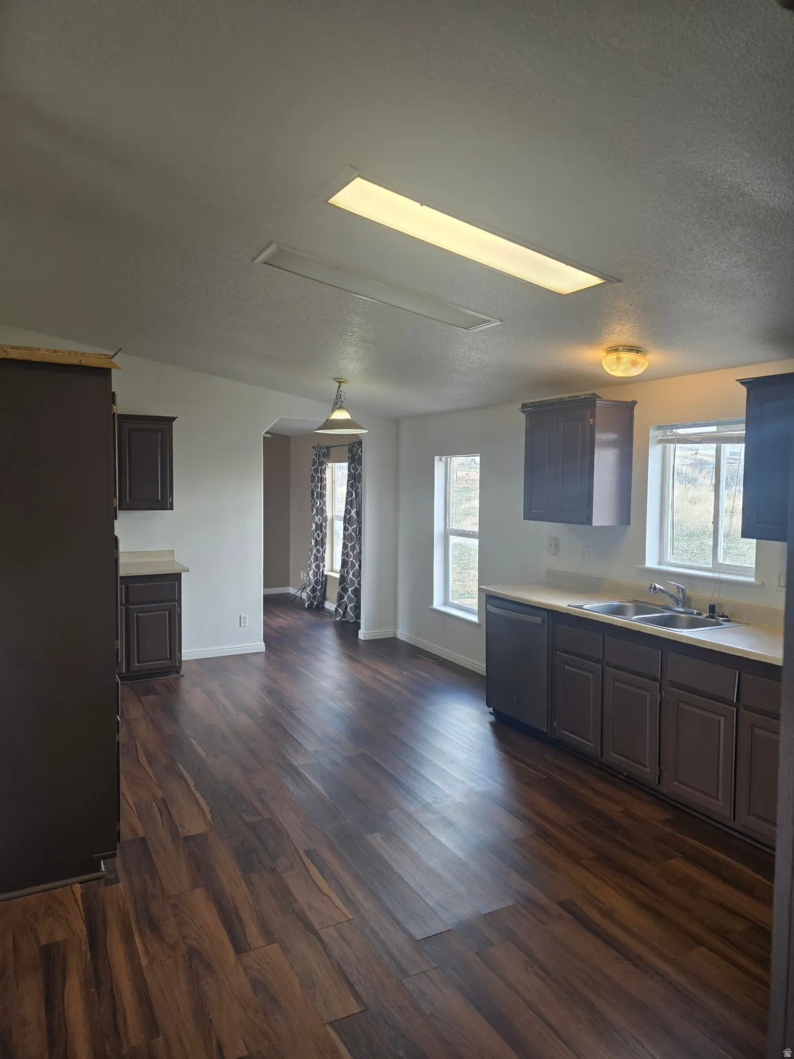 Kitchen featuring light countertops, arched walkways, stainless steel dishwasher, dark wood finished floors, and a textured ceiling