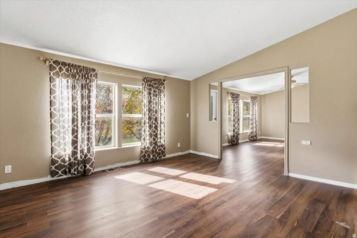 Spare room with healthy amount of natural light, dark wood-style flooring, and vaulted ceiling