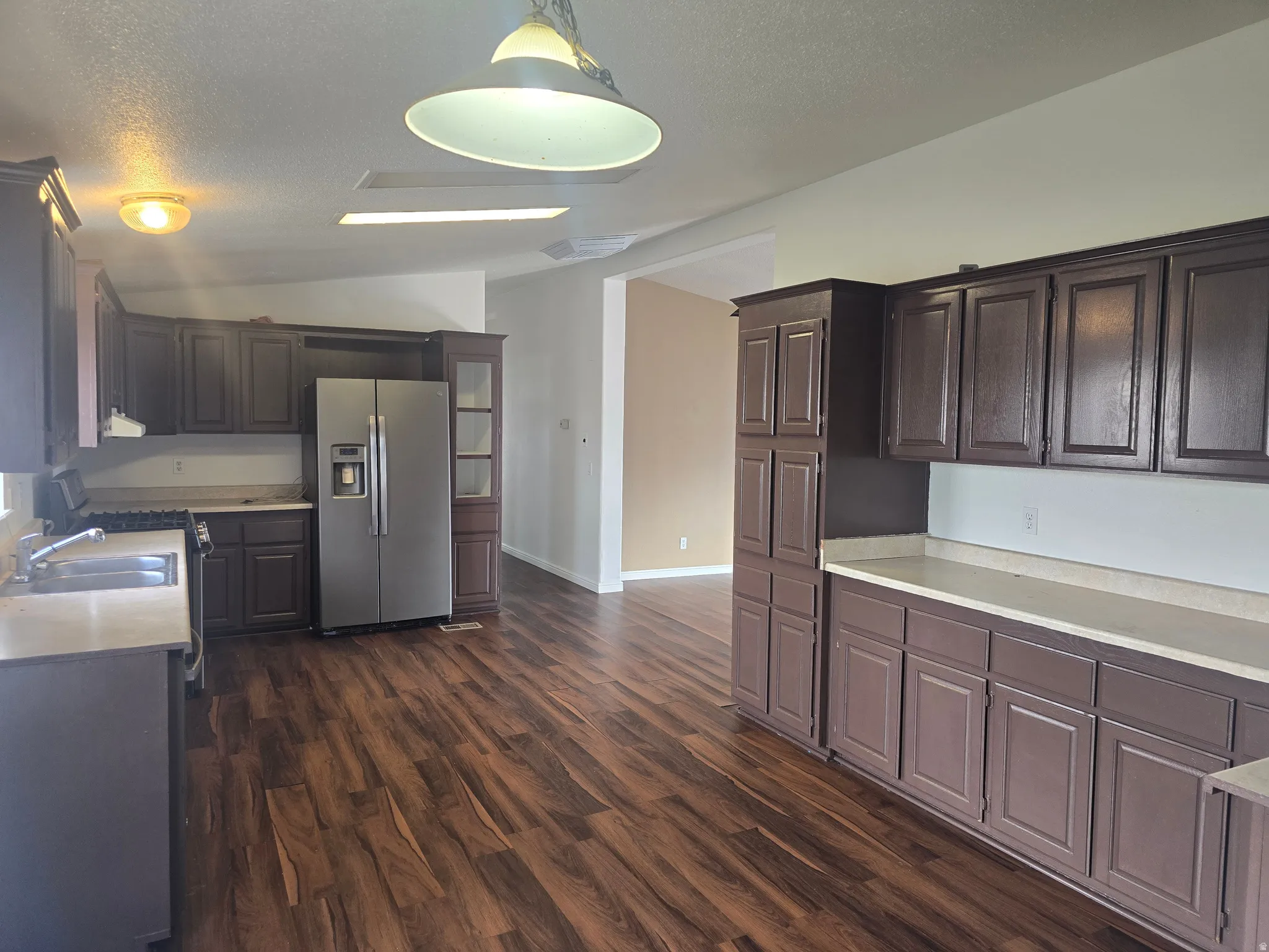 Kitchen with stainless steel appliances, light countertops, decorative light fixtures, dark wood-style floors, and dark wood finish cabinetry