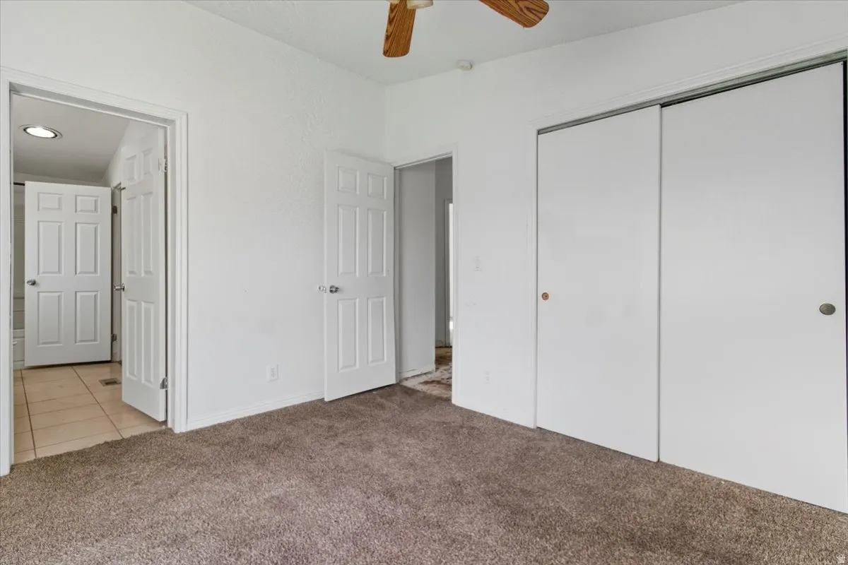 Unfurnished bedroom with light colored carpet, a ceiling fan, and a closet