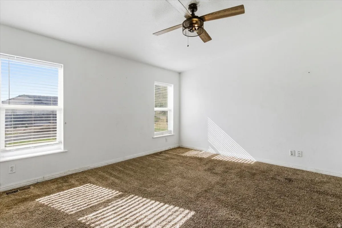Unfurnished room with dark colored carpet and a ceiling fan