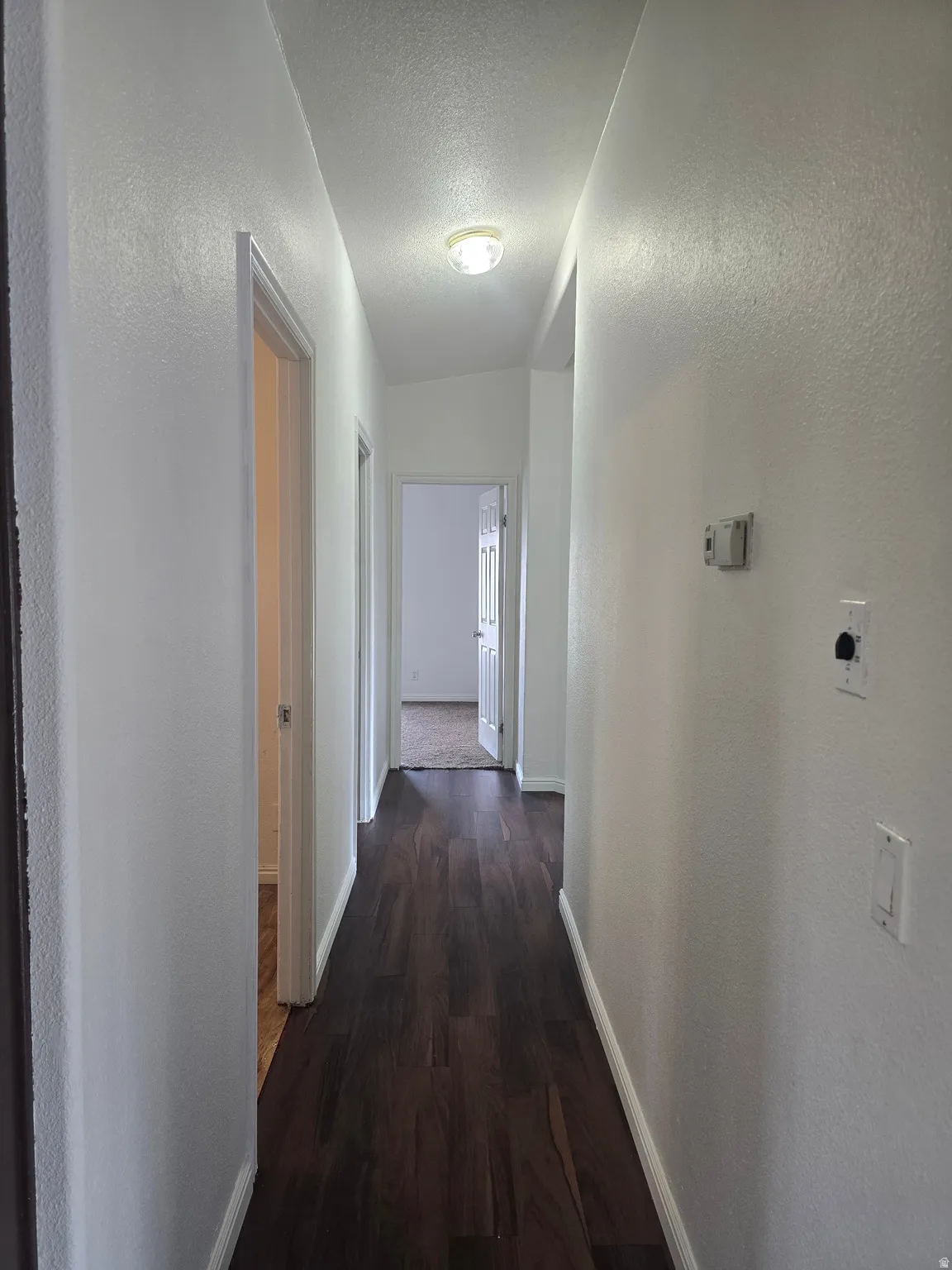 Corridor featuring a textured wall, a textured ceiling, and dark wood-style flooring