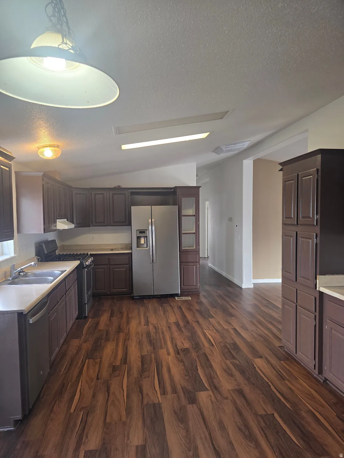 Kitchen featuring stainless steel appliances, light countertops, dark wood finished floors, and dark wood finish cabinetry