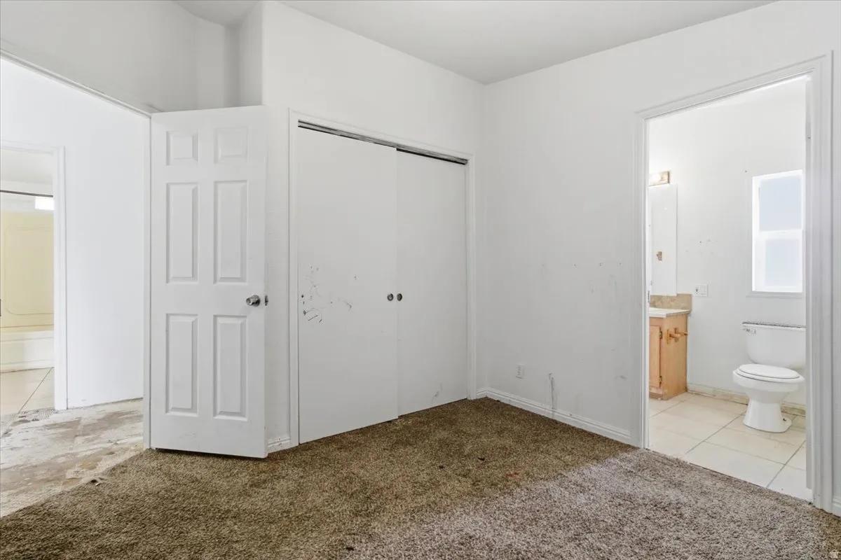 Unfurnished bedroom featuring connected bathroom, light carpet, a closet, and light tile patterned floors