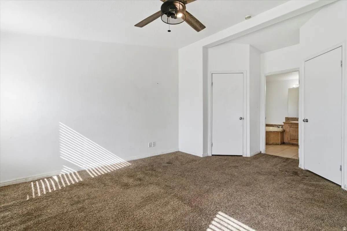 Unfurnished bedroom featuring dark carpet, ensuite bathroom, and ceiling fan