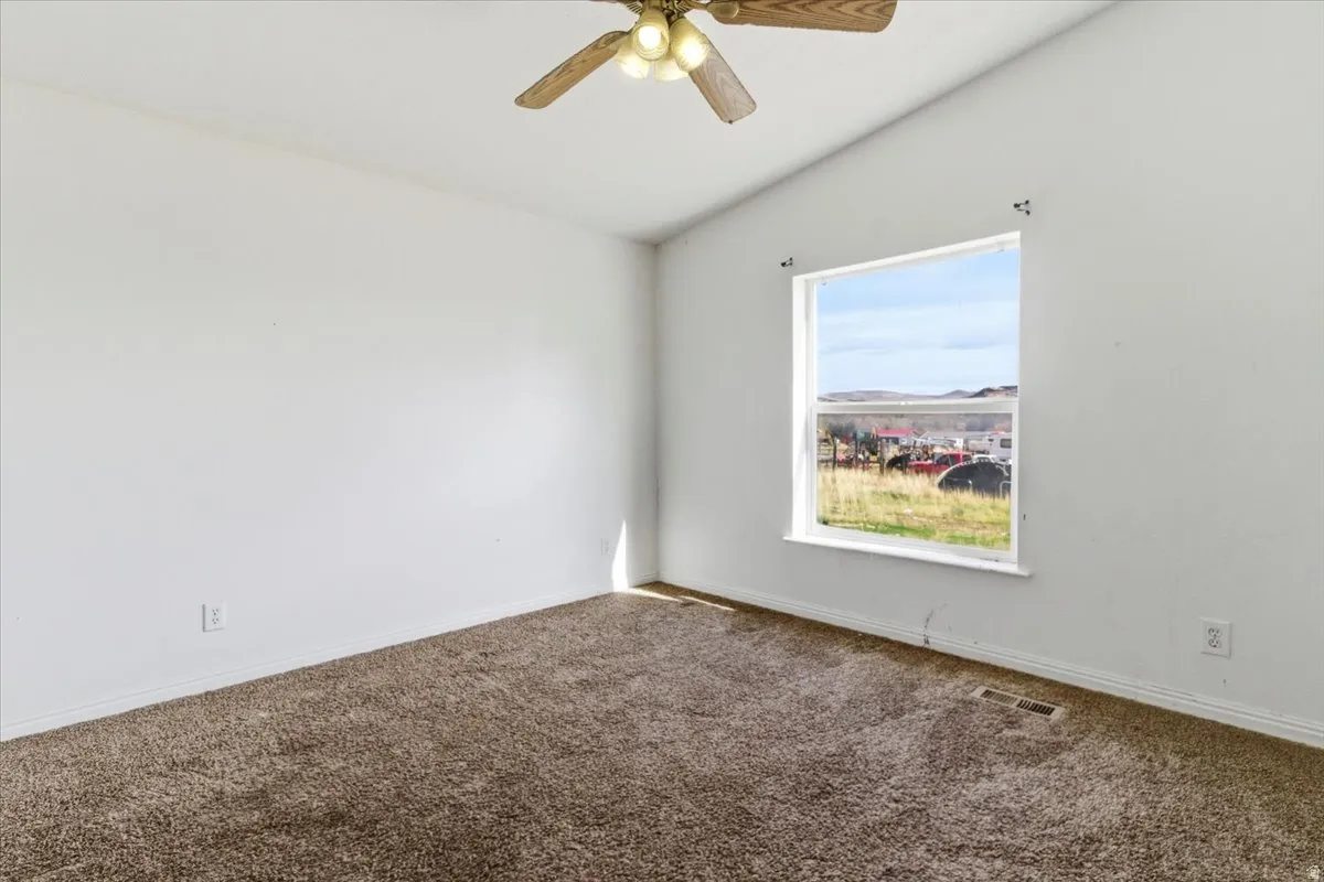 Carpeted spare room featuring ceiling fan and vaulted ceiling