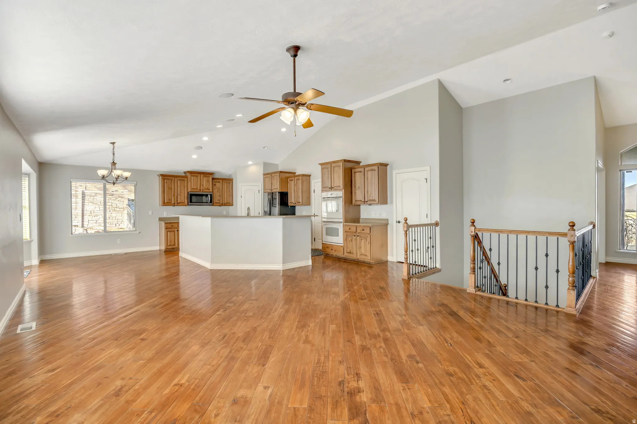 Unfurnished living room featuring healthy amount of natural light, light wood-style flooring, hanging lights, a ceiling fan, and lofted ceiling