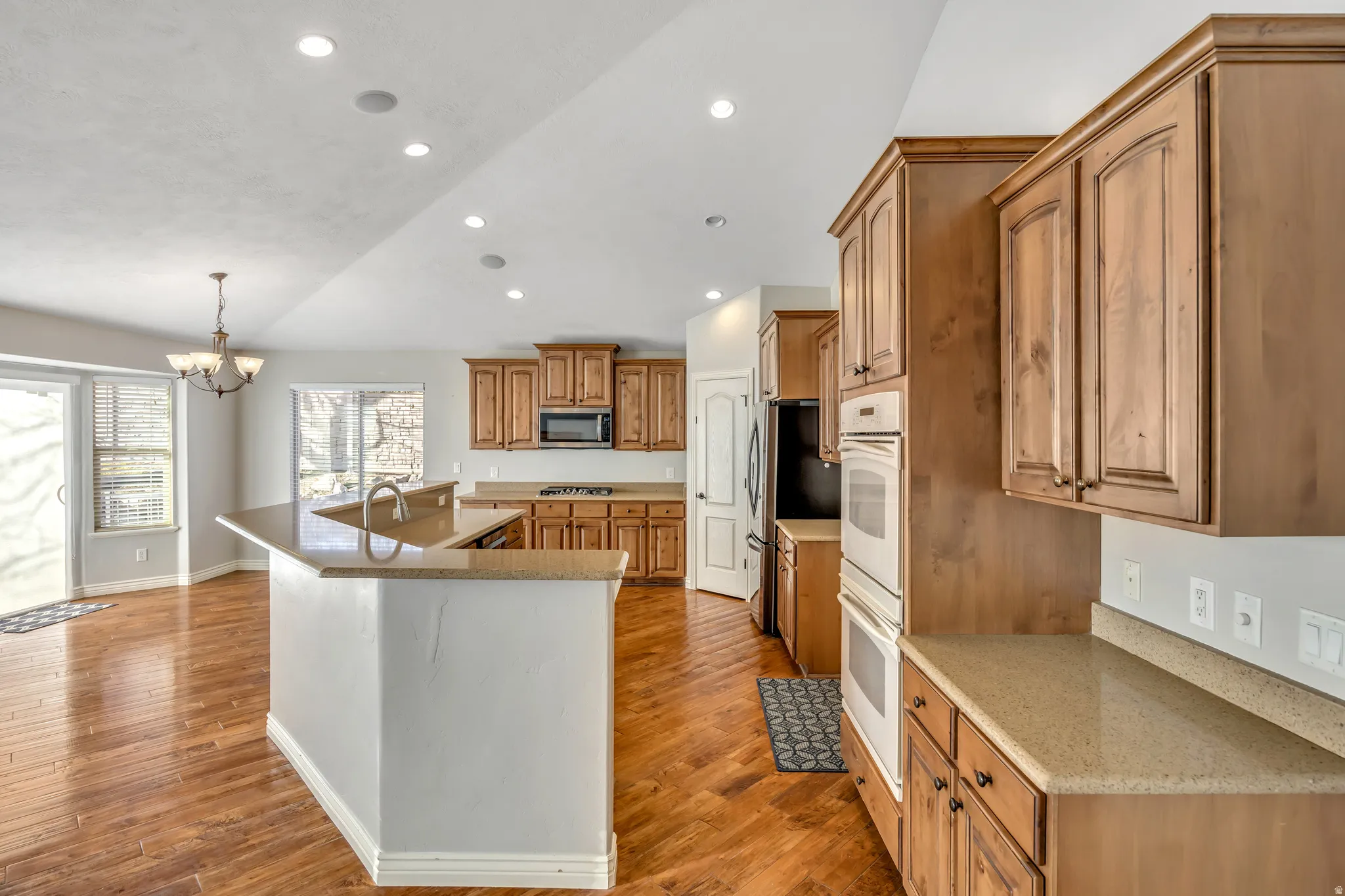 Kitchen with a large island with sink, vaulted ceiling, hanging lights, wood finish cabinetry, and light wood-style floors