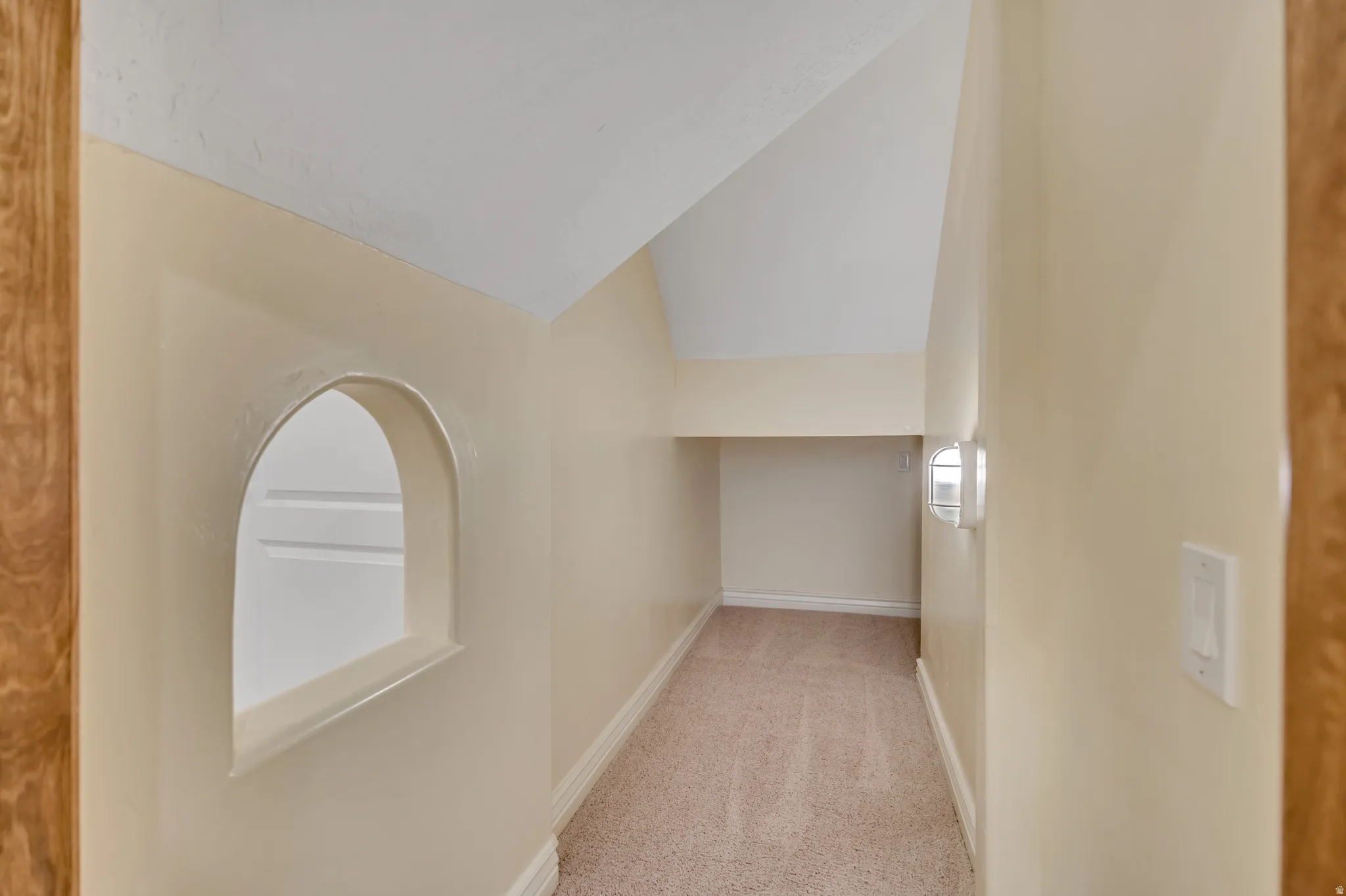 Corridor with vaulted ceiling and light colored carpet