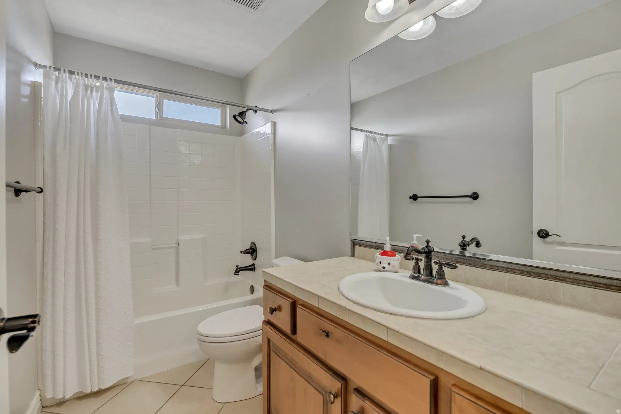Full bathroom with vanity, shower / bath combo with shower curtain, and light tile patterned floors