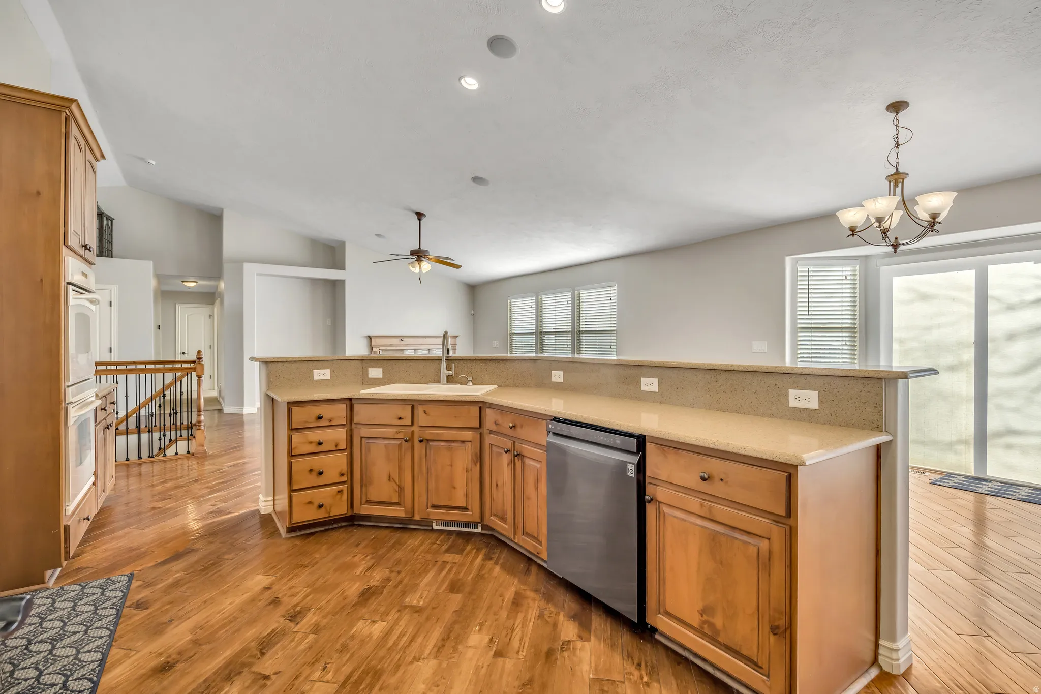 Kitchen with vaulted ceiling, dishwasher, light wood-style flooring, wood finish cabinets, and an island with sink