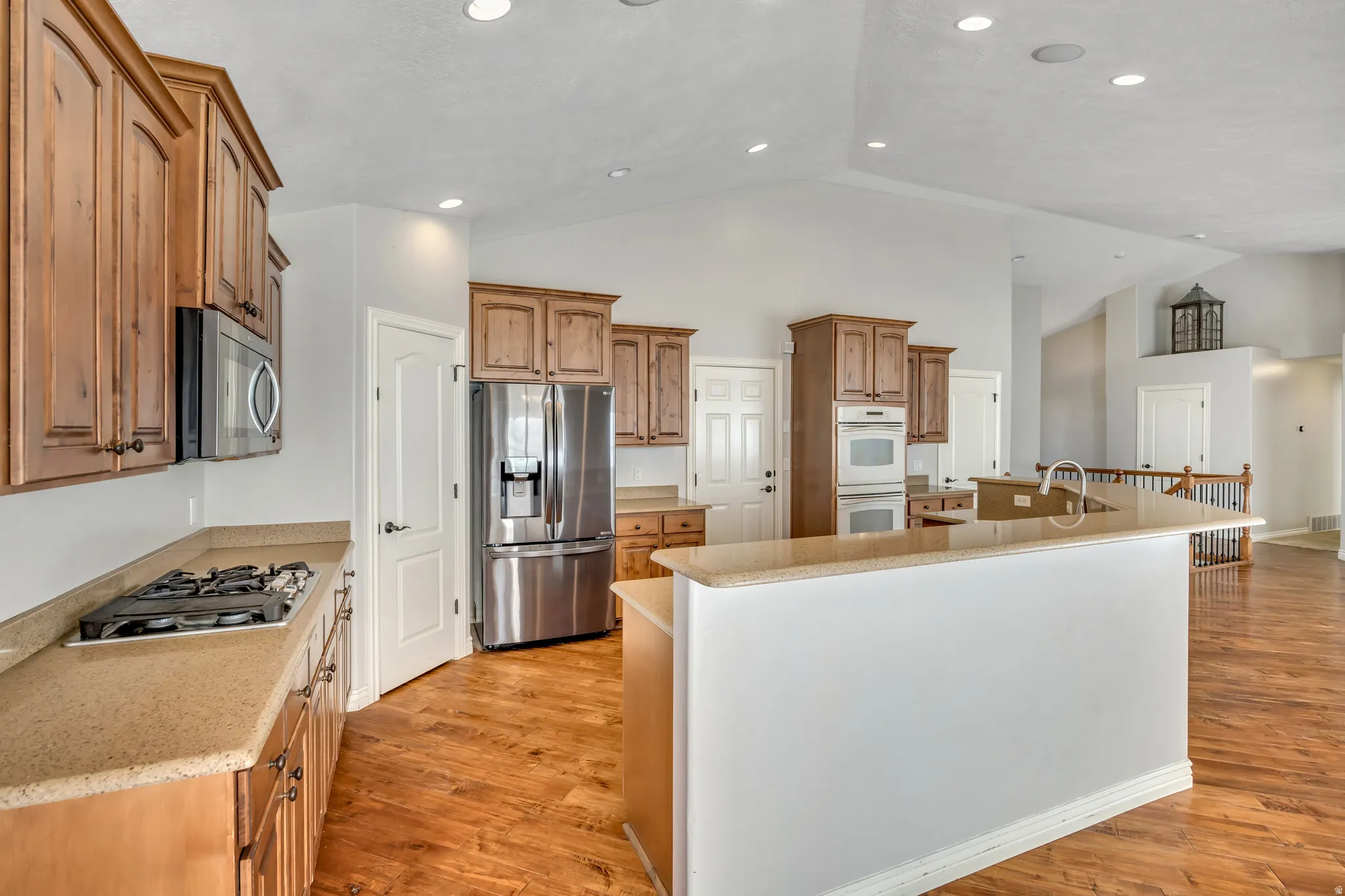 Kitchen featuring a kitchen island with sink, wood finish cabinetry, stainless steel appliances, light wood finished floors, and a high ceiling