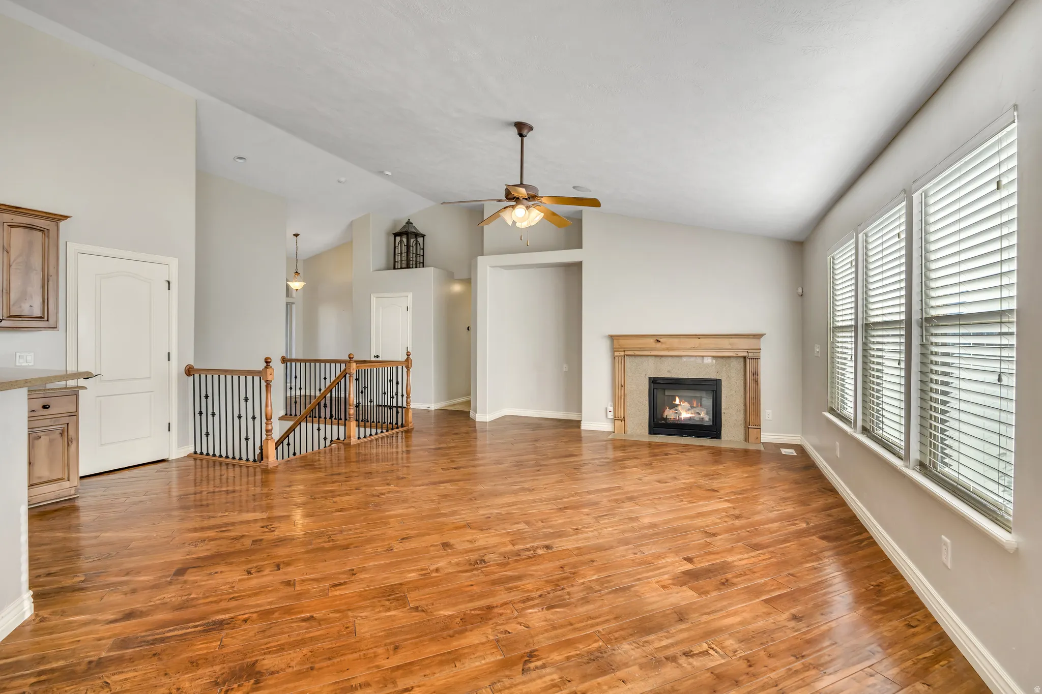 Unfurnished living room featuring light wood finished floors, vaulted ceiling, a high end fireplace, and a ceiling fan