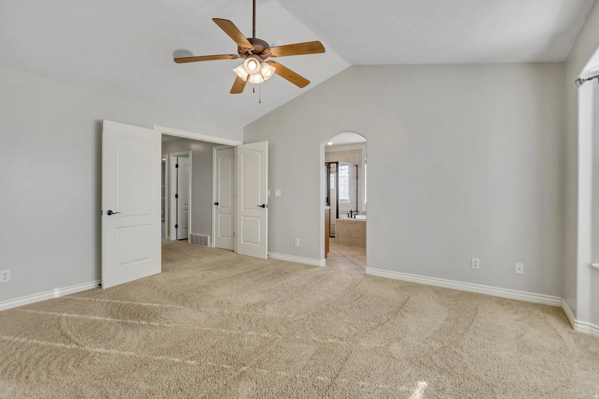 Unfurnished bedroom featuring light carpet, arched walkways, a ceiling fan, and ensuite bathroom