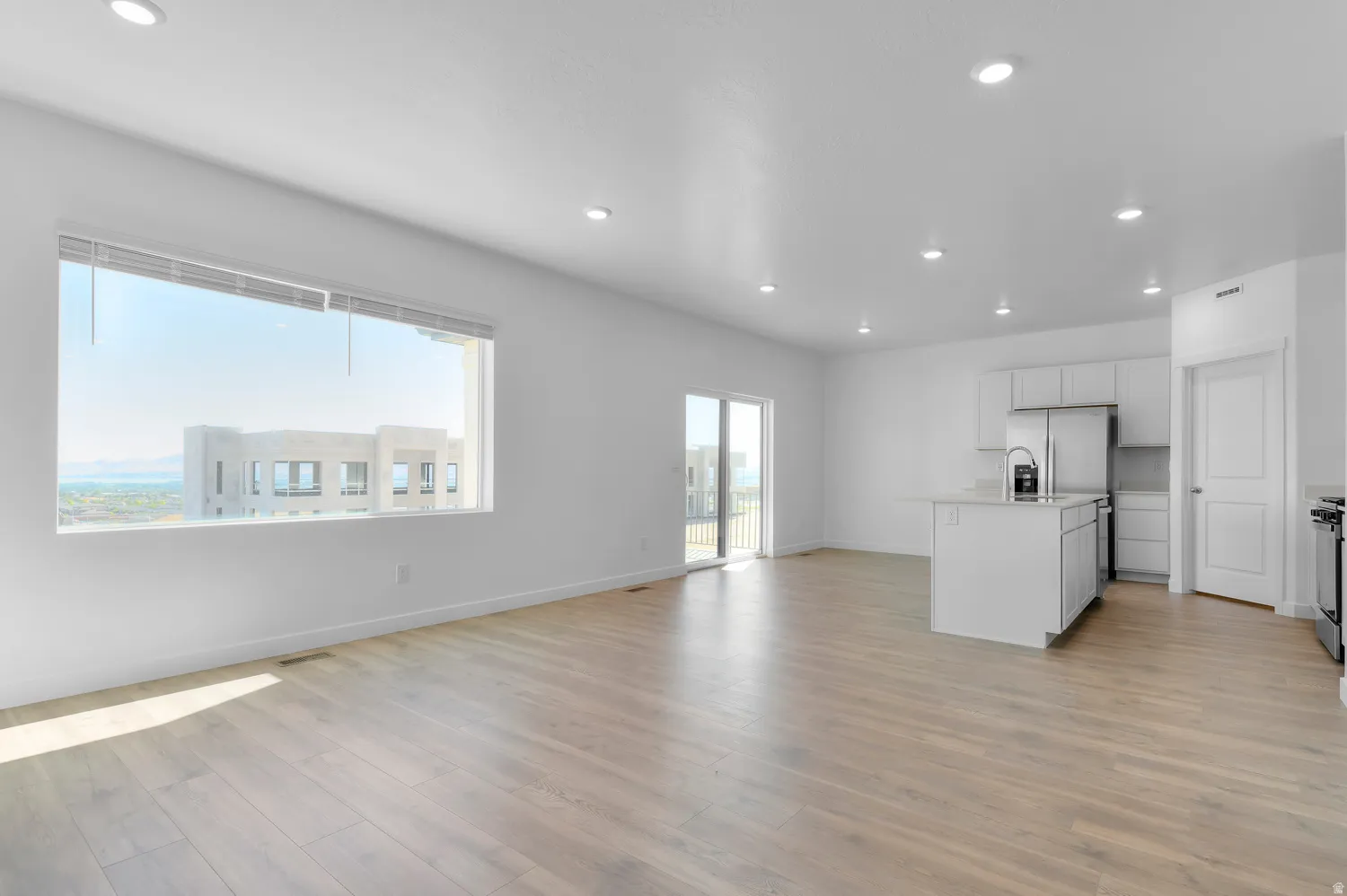 Kitchen featuring open floor plan, light wood finished floors, recessed lighting, a center island with sink, and white cabinets