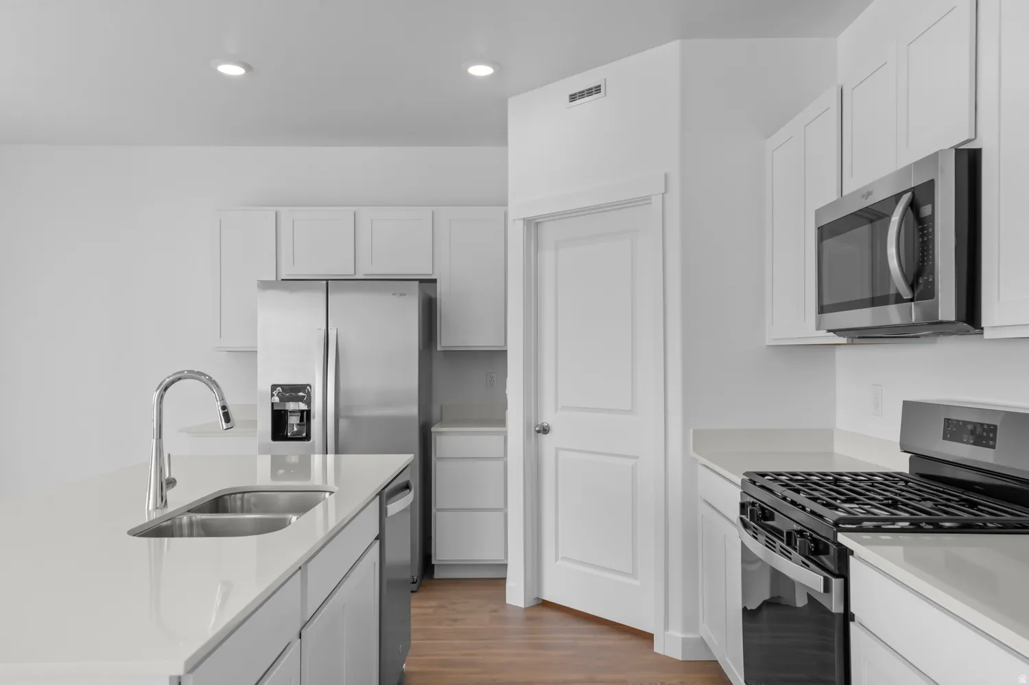 Kitchen with stainless steel appliances, dark wood-style flooring, a center island with sink, white cabinetry, and recessed lighting