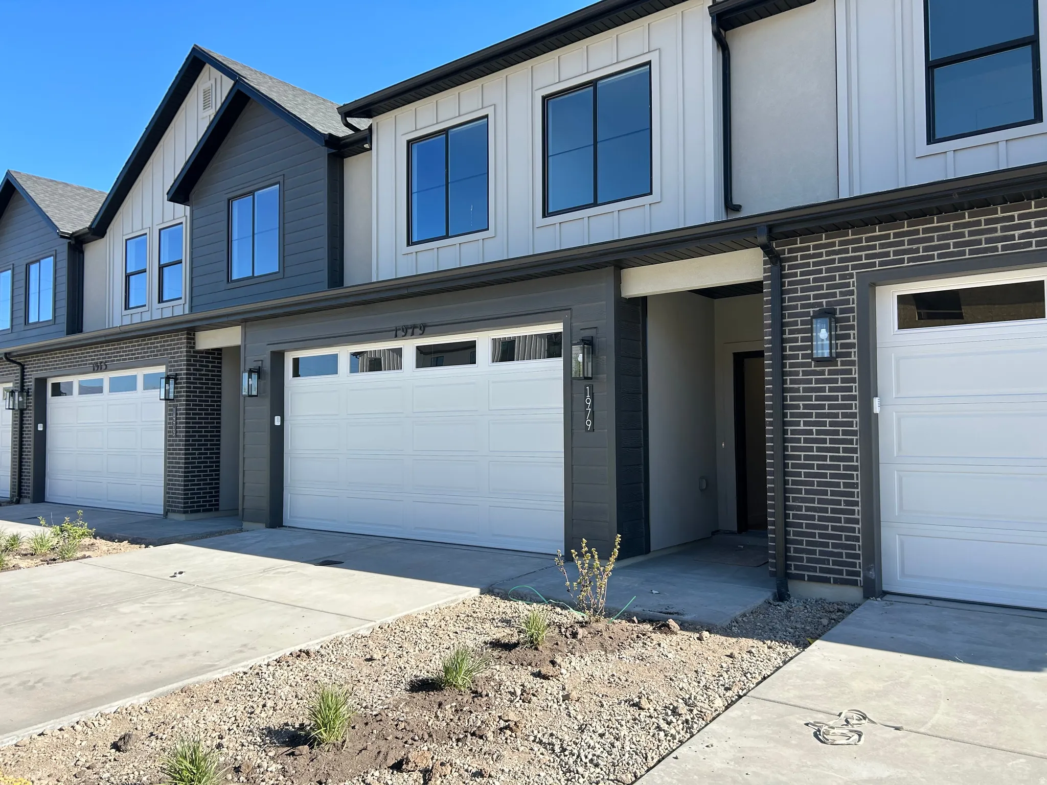 Photos are of model home.Contemporary townhome exterior featuring a white paneled garage door, dark brick accents, and vertical white siding