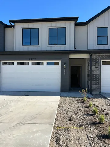 Modern townhome exterior featuring a two-car garage, black-framed windows, vertical white siding, and a contrasting dark brick accent