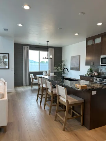 Spacious open-concept living area featuring a large kitchen island with a dark granite countertop, wood-finish flooring, recessed lighting, and dark wood cabinetry with frosted glass accents