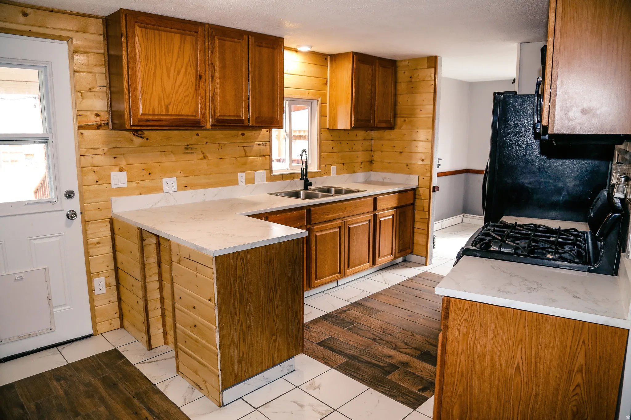 Kitchen with wood finish cabinetry, wood walls, gas stove, light countertops, and a peninsula