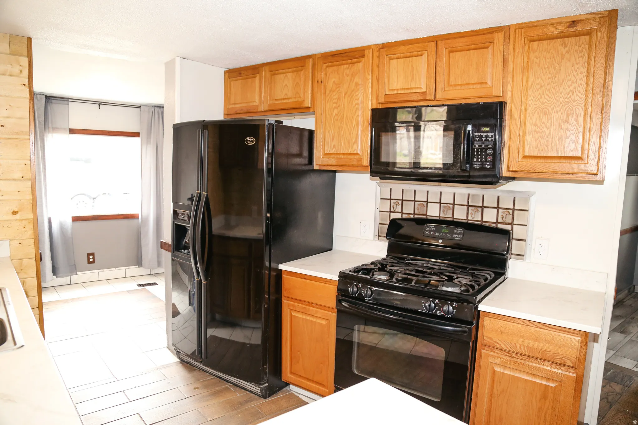 Kitchen with black appliances, light countertops, wood finish cabinets, and light wood-style floors
