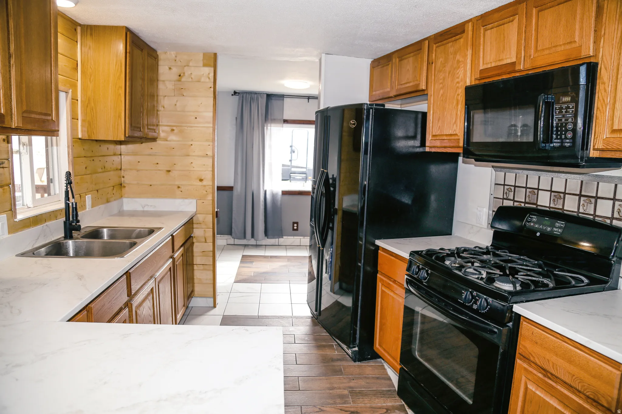 Kitchen with black appliances, wood finish cabinets, dark wood-type flooring, decorative backsplash, and light stone counters