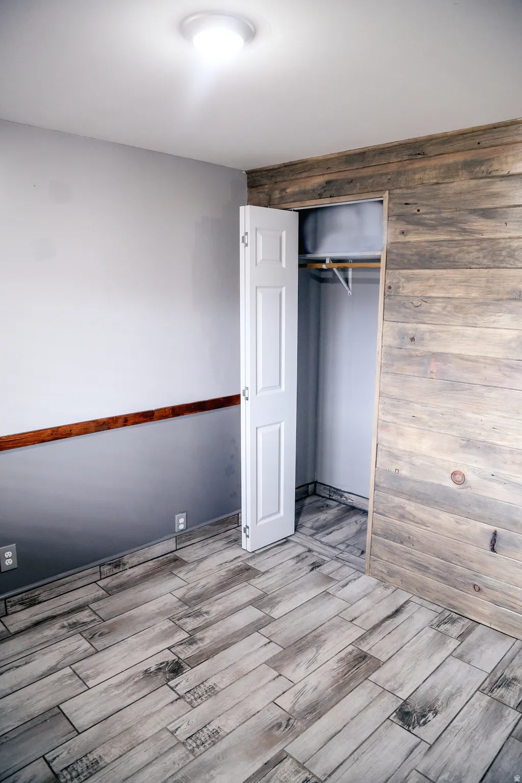 Unfurnished bedroom featuring wood finish floors, a closet, and wood walls