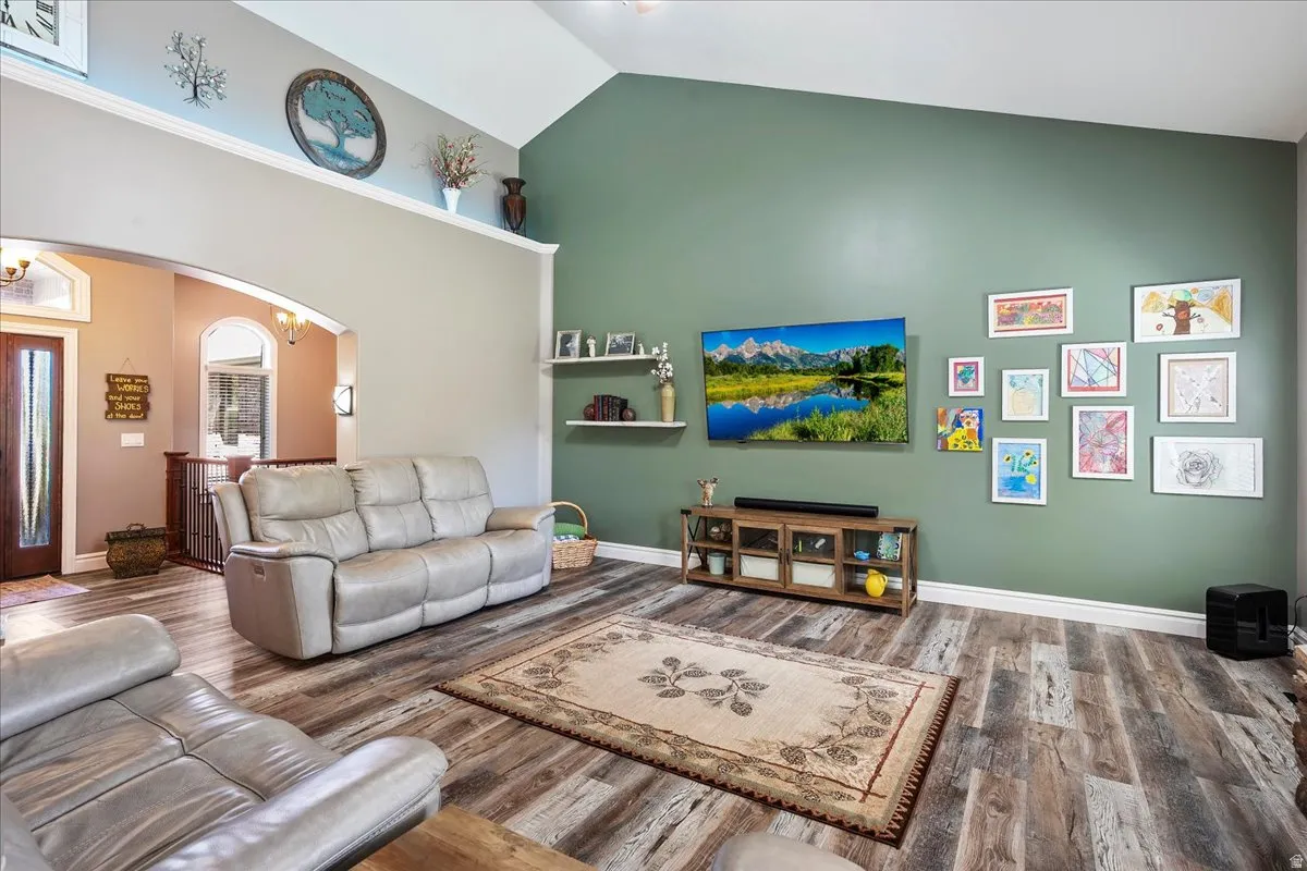 Living room with arched walkways, wood finished floors, and vaulted ceiling