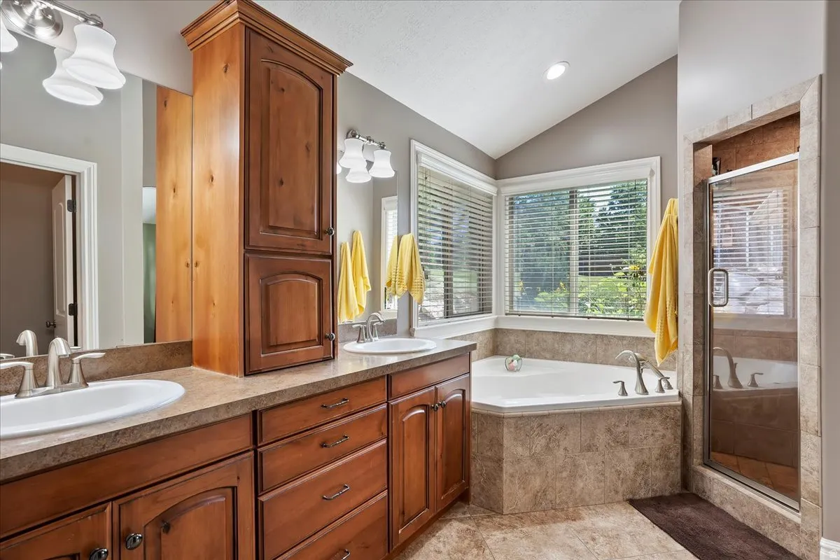Bathroom featuring double vanity, a stall shower, vaulted ceiling, and a garden tub