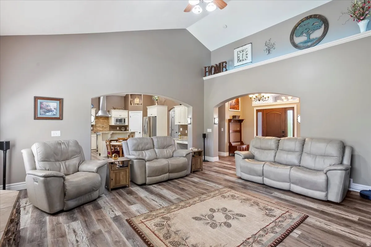 Living area with arched walkways, a ceiling fan, wood finished floors, and vaulted ceiling