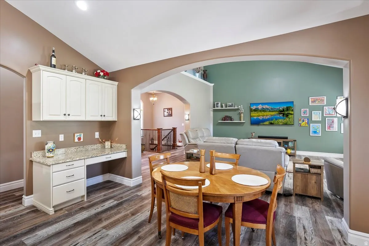 Dining area with built in desk, lofted ceiling, dark wood-type flooring, and arched walkways