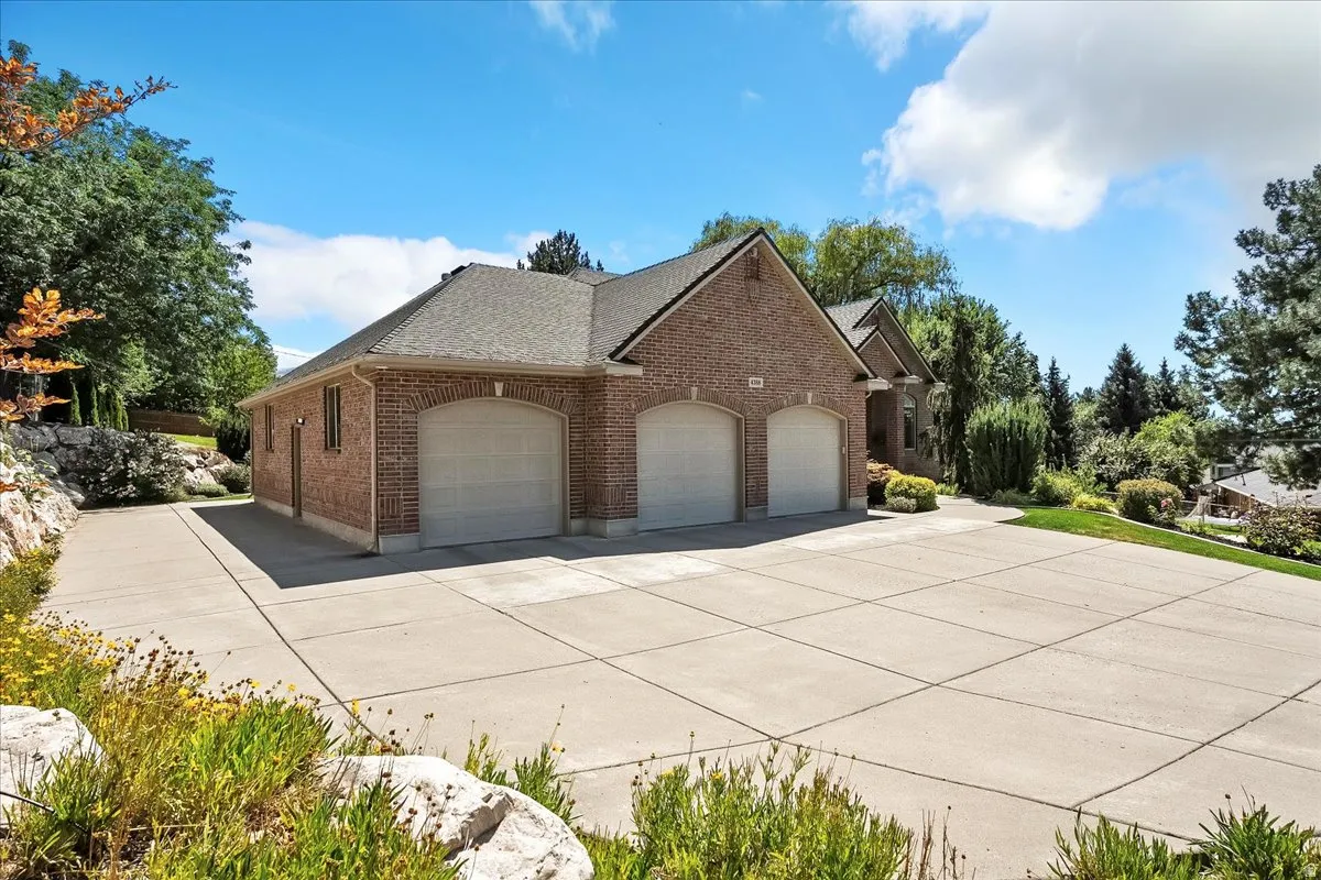 View of side of property with brick siding, an attached garage, a shingled roof, and concrete driveway