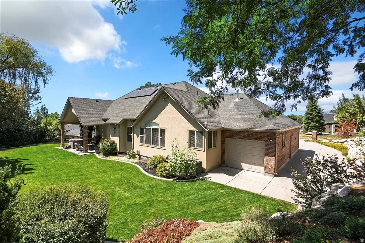 Rear view of house featuring roof mounted solar panels, a yard, an attached garage, a shingled roof, and stucco siding