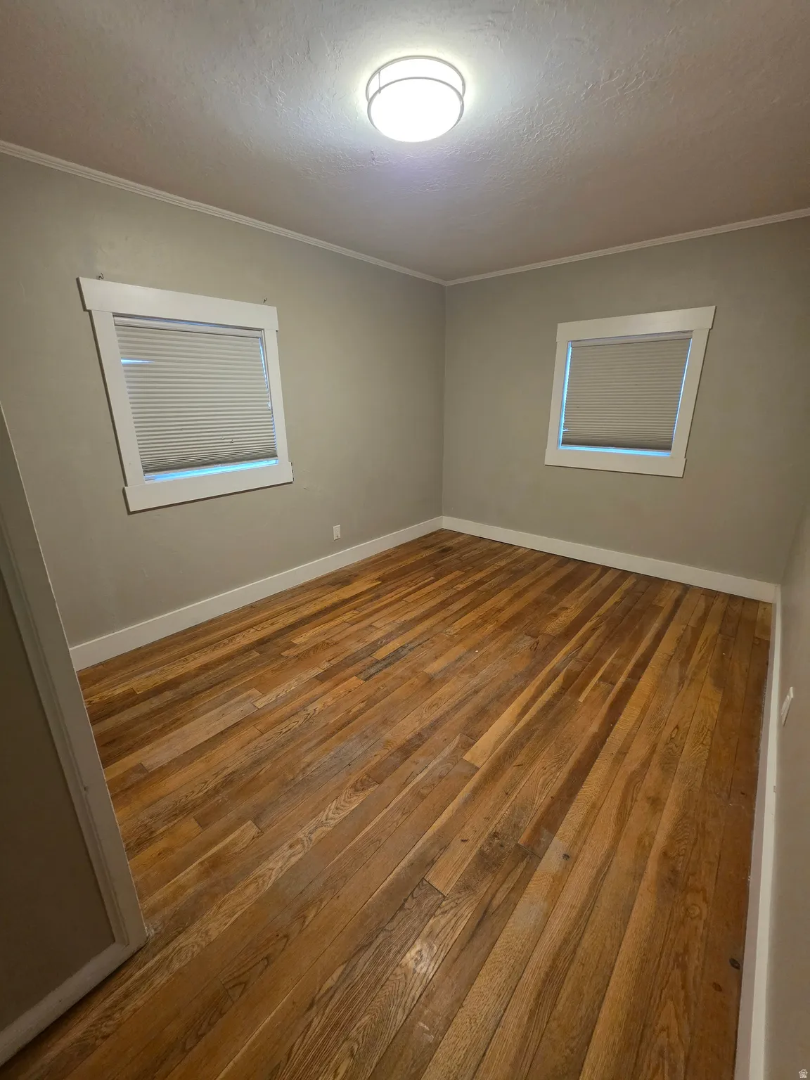 Empty room featuring hardwood / wood-style floors, a textured ceiling, and crown molding
