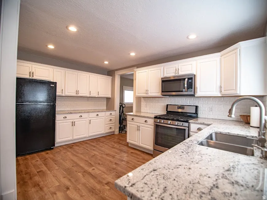 Kitchen with stainless steel appliances, white cabinetry, light stone counters, a textured ceiling, and light wood-style floors