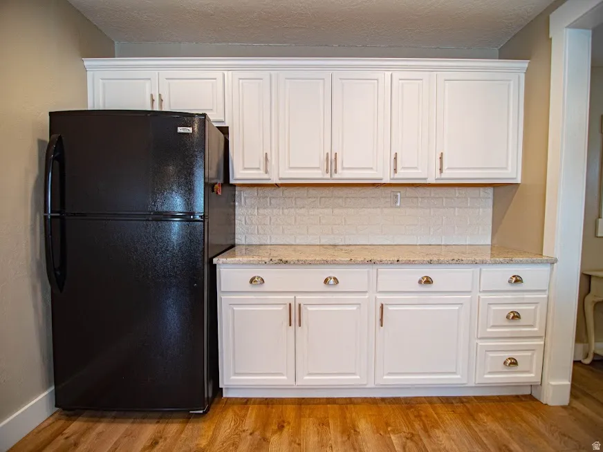 Kitchen featuring white cabinets, freestanding refrigerator, light stone countertops, tasteful backsplash, and a textured ceiling