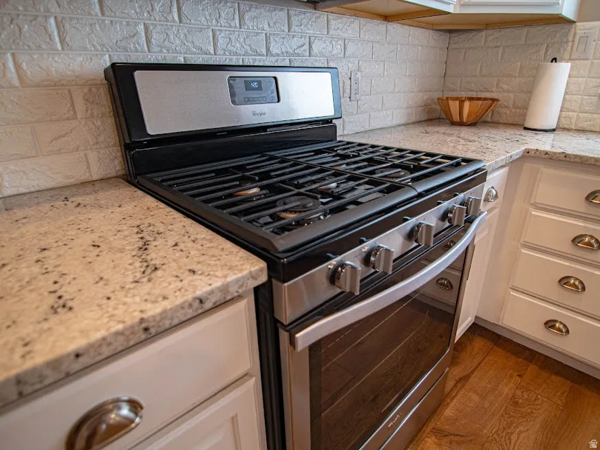 Kitchen with stainless steel range with gas stovetop, light stone countertops, and decorative backsplash