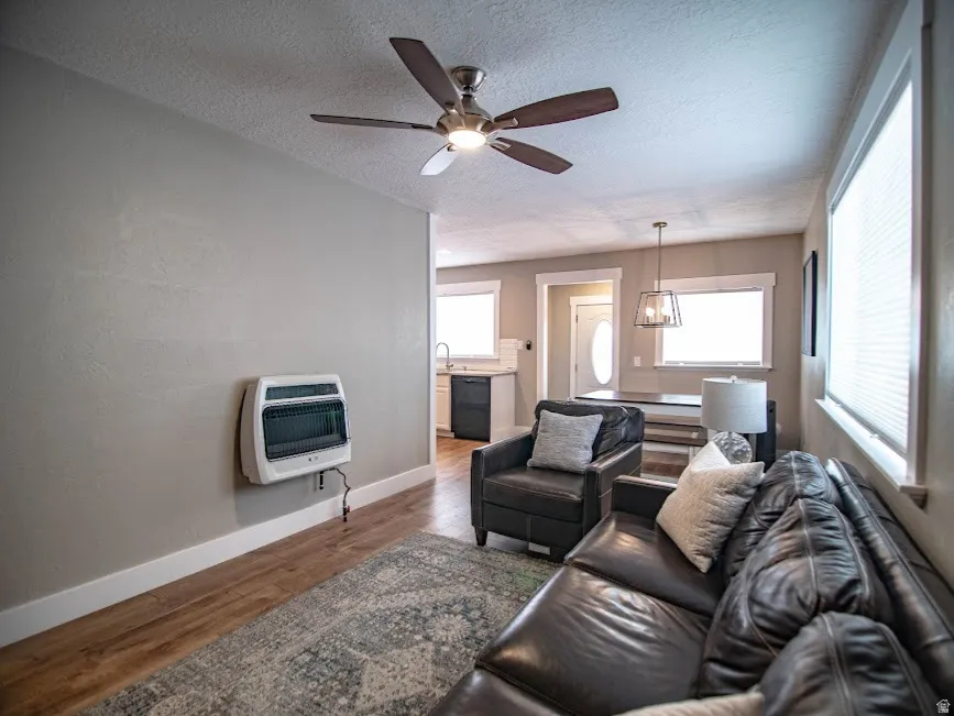 Living area with dark wood-type flooring, heating unit, a textured ceiling, and ceiling fan