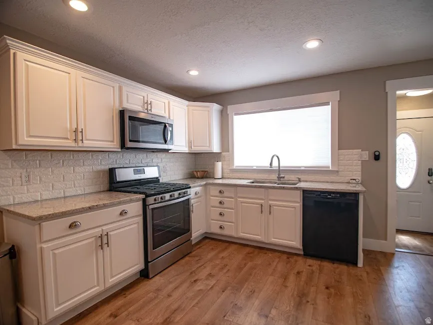 Kitchen with stainless steel appliances, white cabinetry, light stone countertops, light wood-style floors, and backsplash