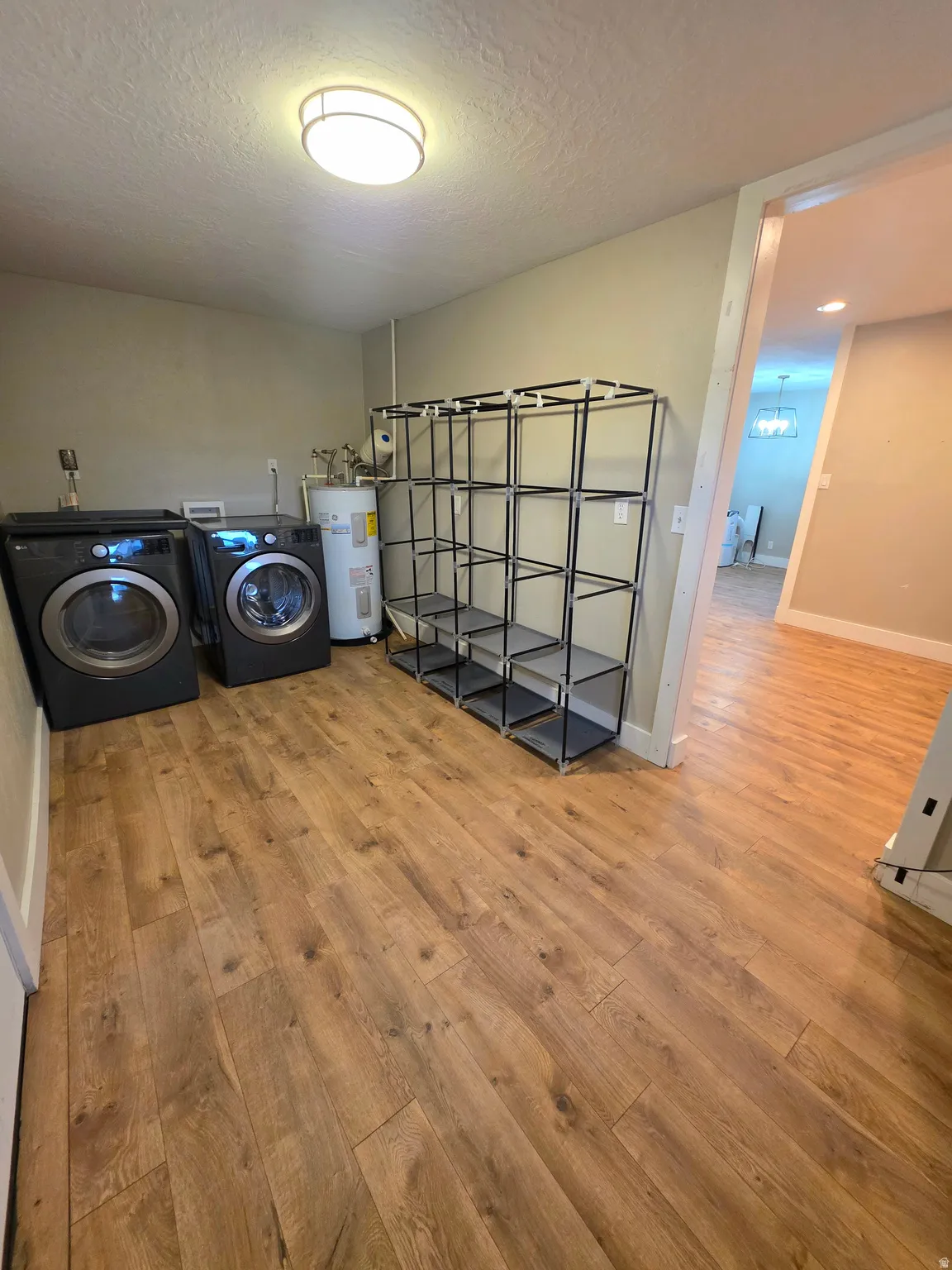 Laundry room with light wood-style floors, electric water heater, a textured ceiling, and separate washer and dryer
