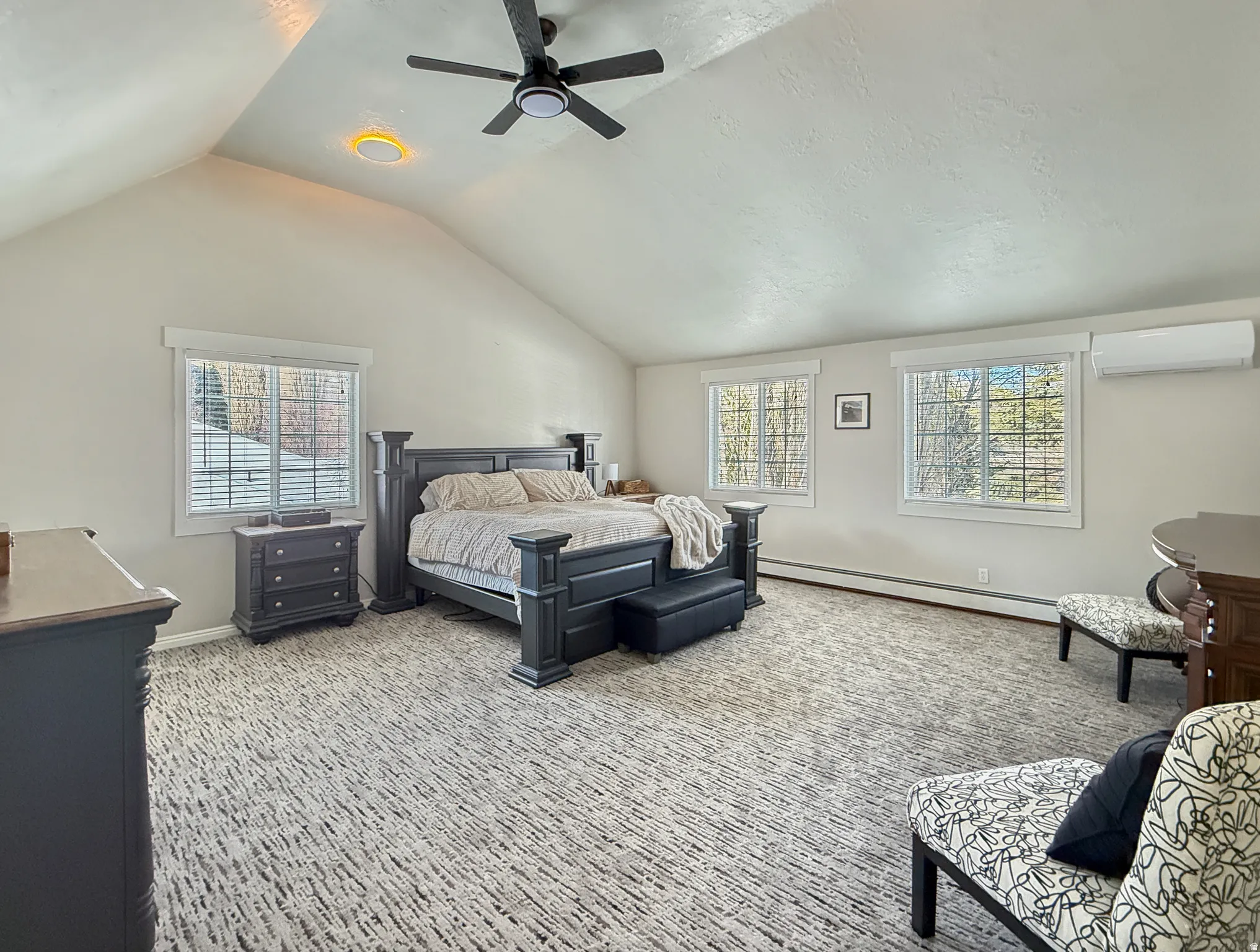Bedroom with a baseboard heating unit, ceiling fan, multiple windows, and light carpet