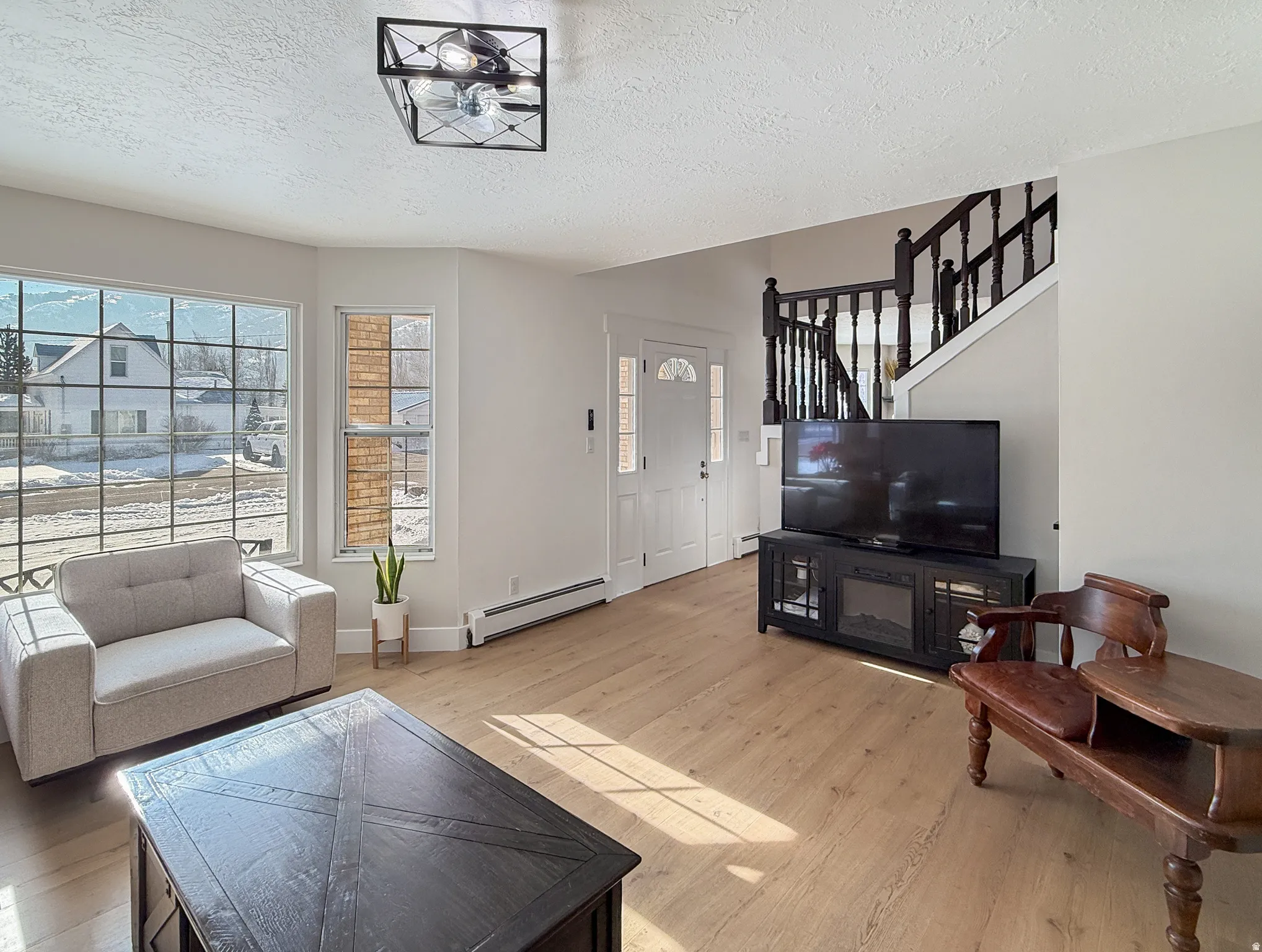 Living room featuring light wood-type flooring, a baseboard radiator, and a textured ceiling