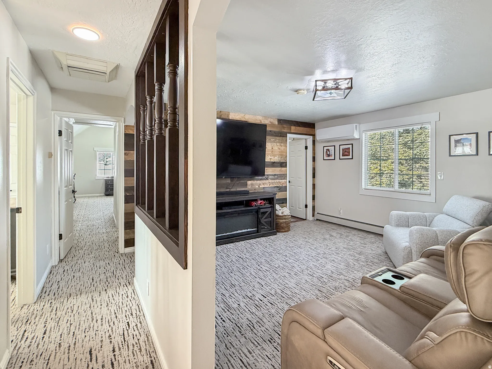 Living room featuring a textured ceiling, a baseboard radiator, cooling unit, light carpet, and healthy amount of natural light