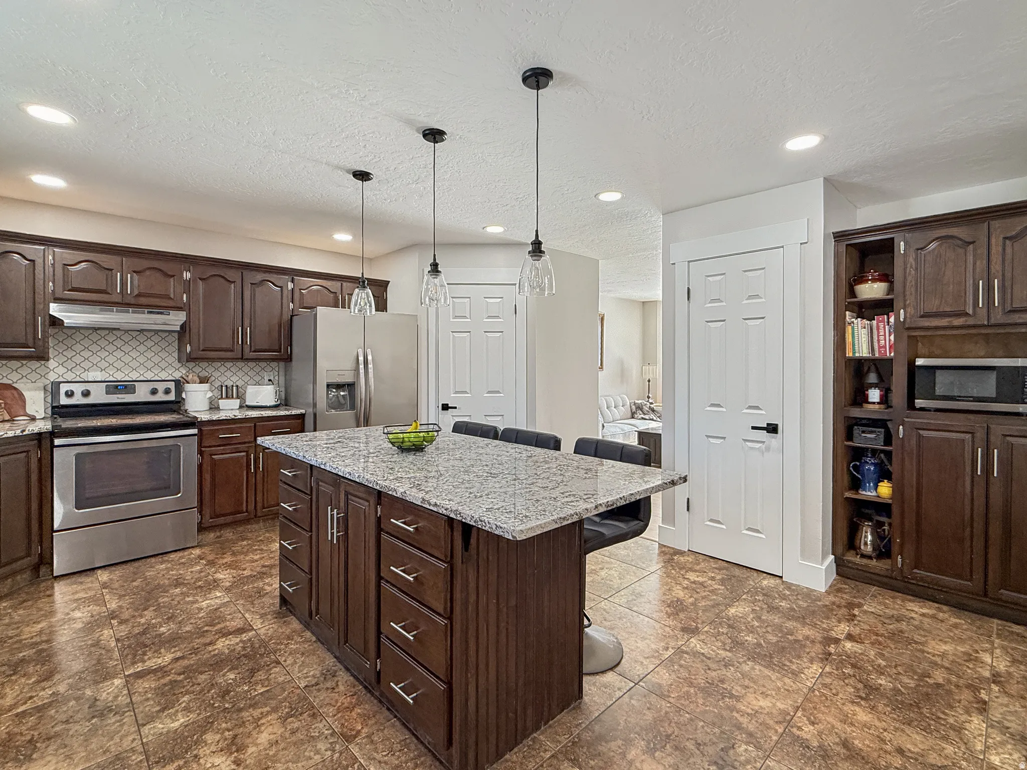 Kitchen with a breakfast bar, dark wood finish cabinets, stainless steel appliances, a center island, and a textured ceiling