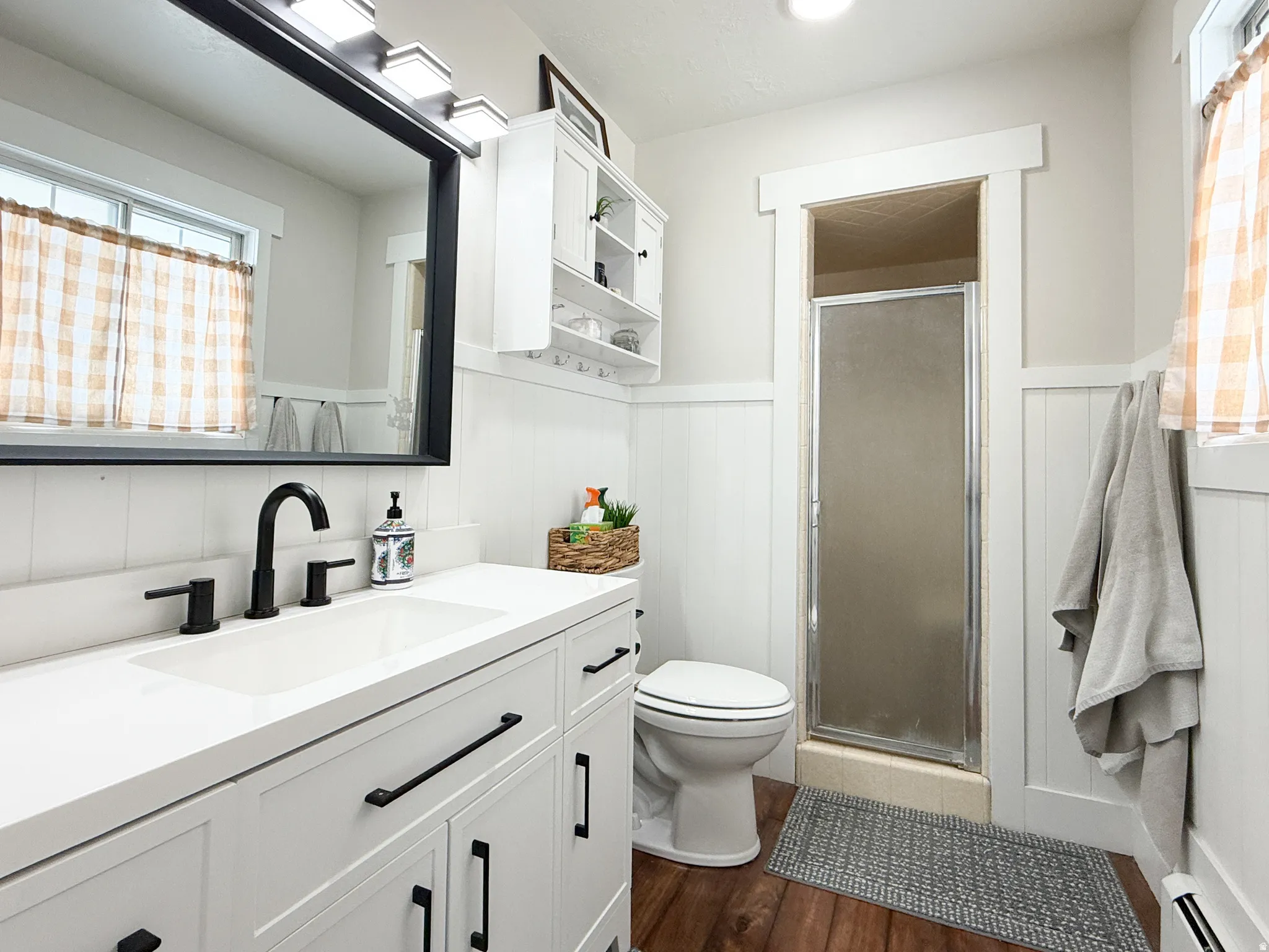 Bathroom with vanity, a stall shower, a wainscoted wall, dark wood-style floors, and a baseboard heating unit