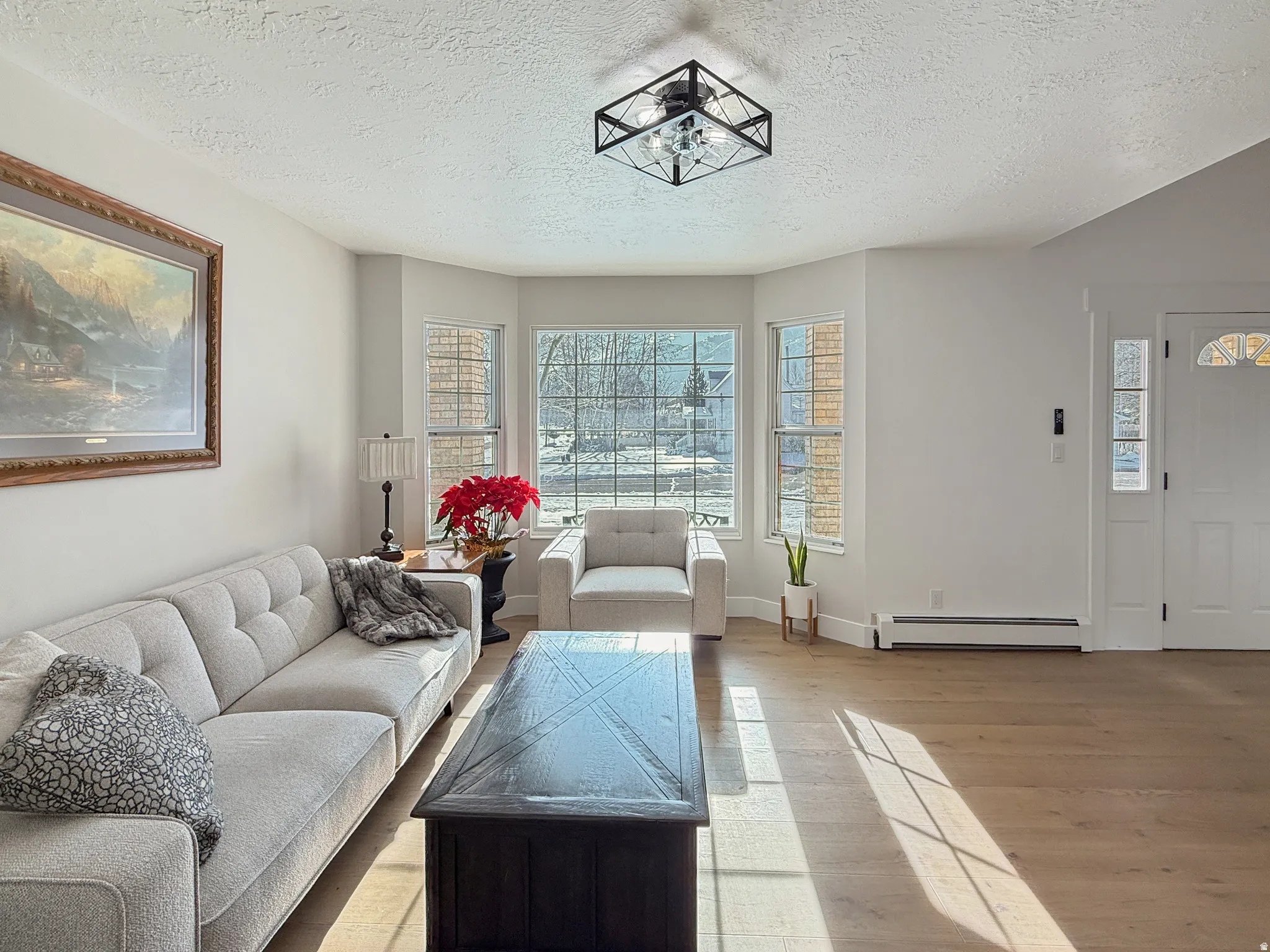 Living area featuring light wood-type flooring, a baseboard radiator, and a textured ceiling