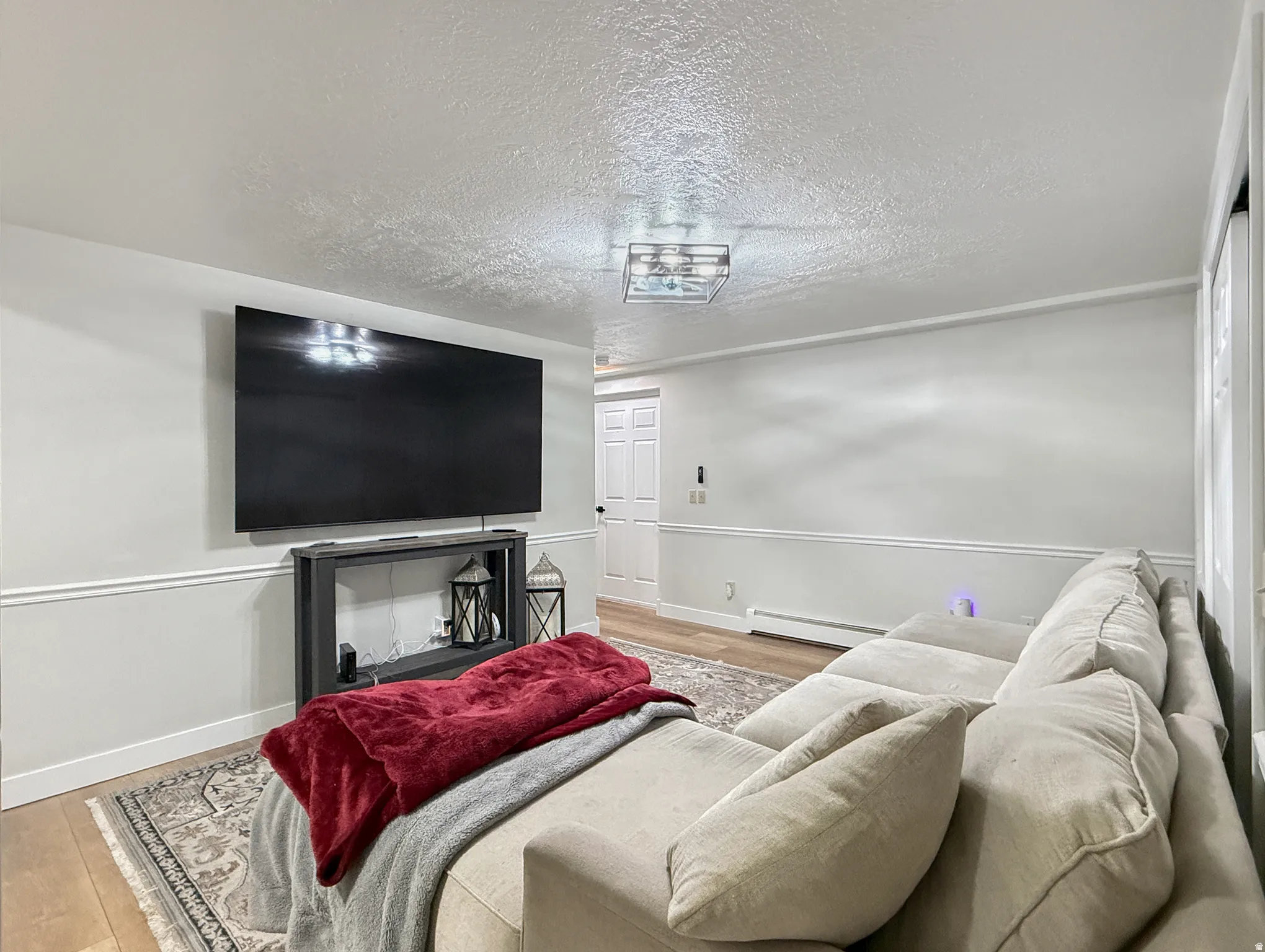 Living room featuring a textured ceiling, light wood finished floors, and a baseboard heating unit