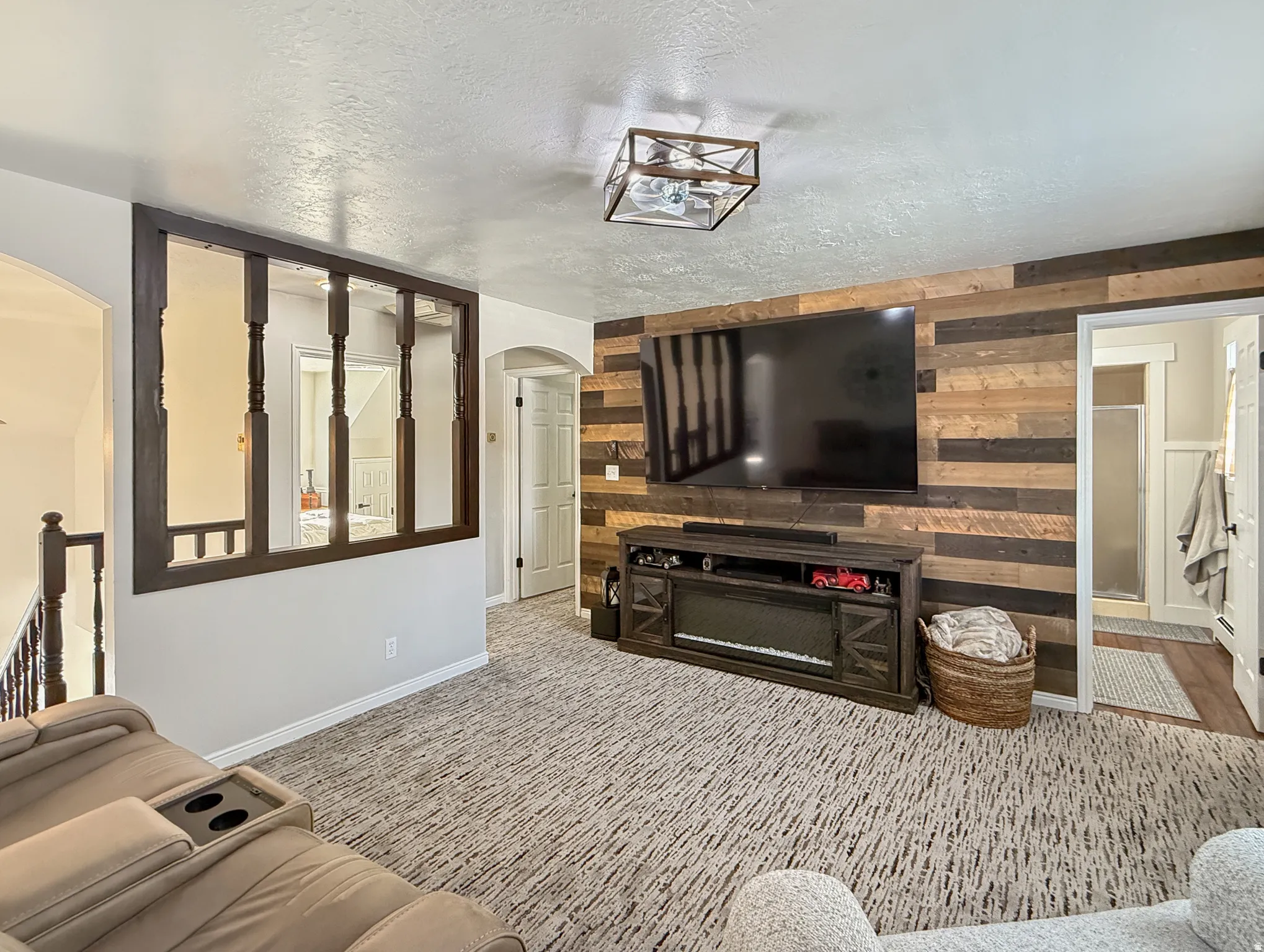 Living area featuring arched walkways, a textured ceiling, wooden walls, and carpet flooring